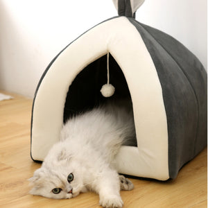 White cat playing with a toy inside a gray and white pet house on a wooden floor.