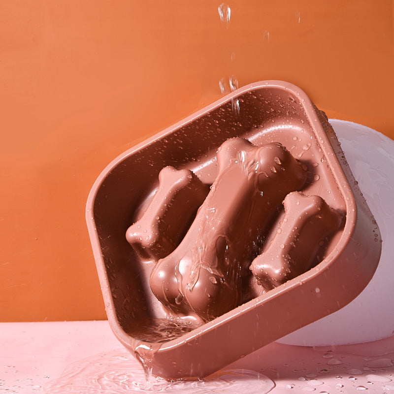 Chocolate mold with bone-shaped cavities on a pink surface against an orange background