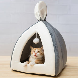 Cat inside a gray and white pet bed with bunny ears on a wooden surface.
