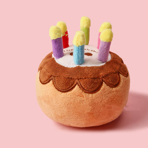 Plush toy resembling a birthday cake with colorful candles on a pink background