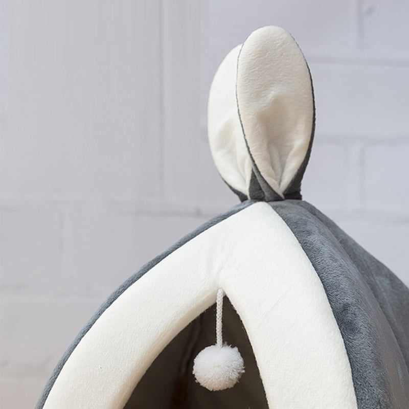 Gray and white pet bed with a pom-pom hanging from it against a gray background