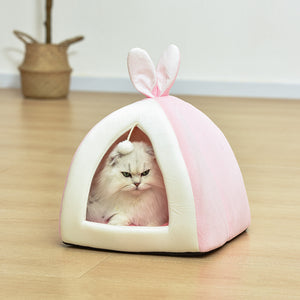 Cat inside a pink and white pet tent with bunny ears on a wooden floor.