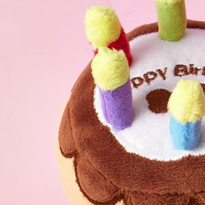 Plush birthday cake toy with candles on a pink background